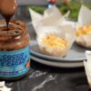 Vasetto aperto con cucchiaino che prende la crema ,piatti con sopra mini torte al cocco