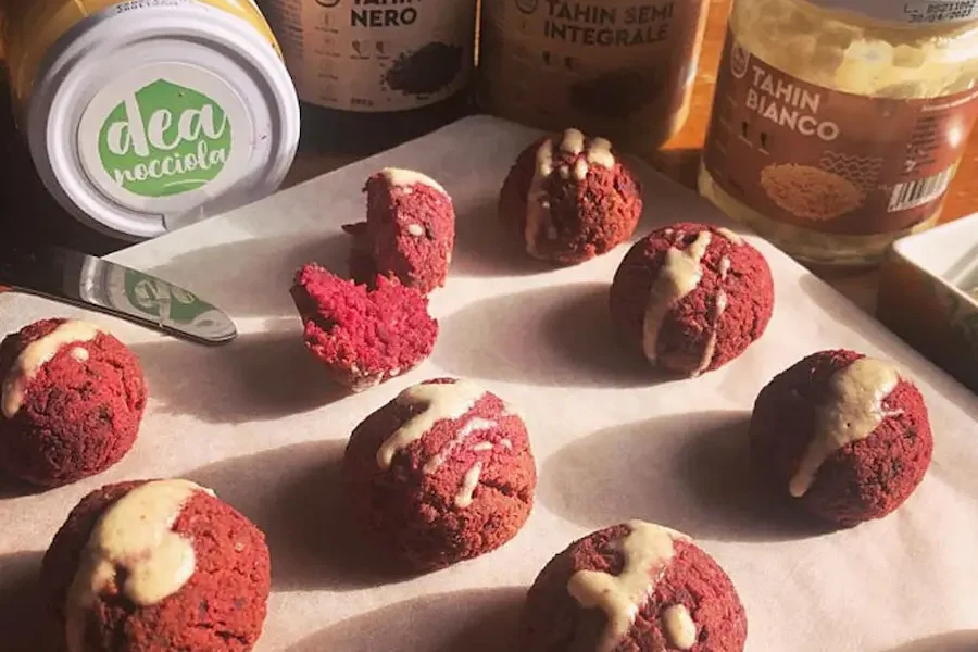 Felafel di barbabietola e arachidi con salsa alla tahin su un tagliere e dietro le creme arachidi 100%