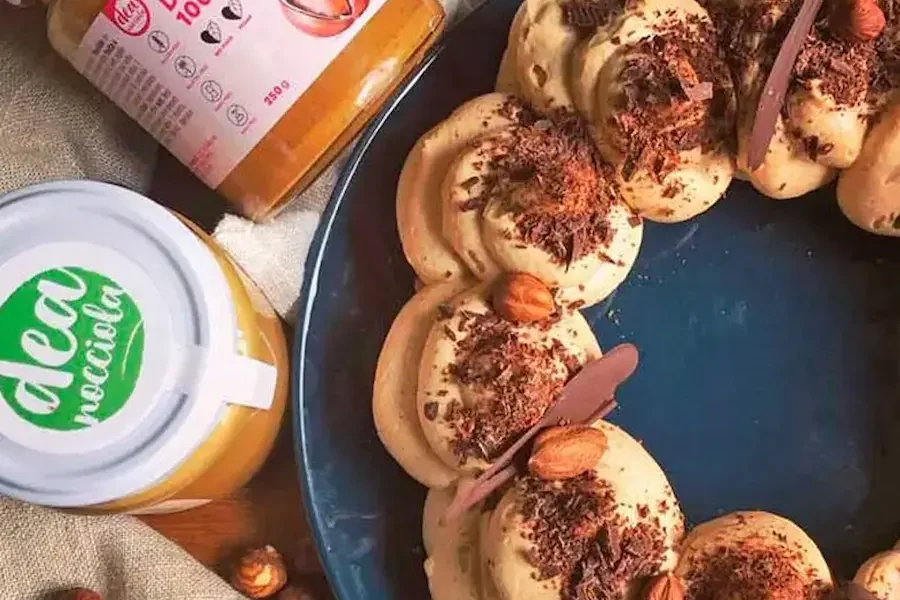 Pavlova alla nocciola e caffè su un piatto e vasetti di creme di nocciola 100%