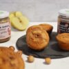 2 vasetti di crema (nocciola e 3 ingredienti nocciola 70%) un piatto con muffin , sul tavolo una mela e delle nocciole