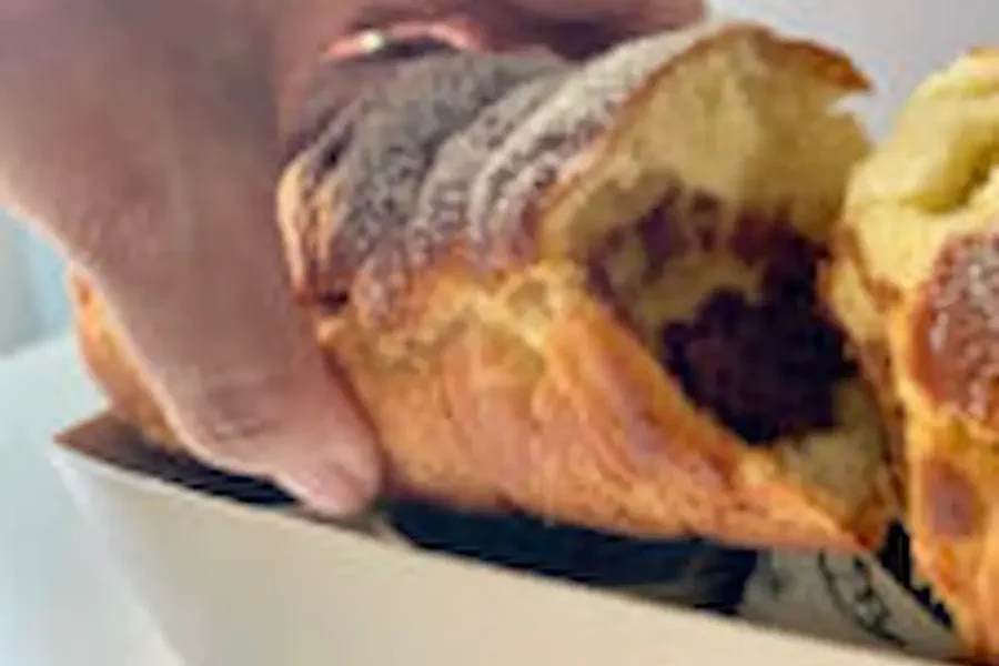 Una mano tiene un pan brioche, all' interno di una scatola di cartone,aperto dove all interno possiamo vedere il suo ripieno di crema spalmabile classica al latte.