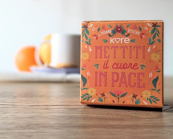 una scatola di tisana kore arancione con scritta mettiti il cuore in pace e sfondo sfuocato