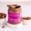 close up di un barattolo di crema crunchy nocciola e cacao aperto su cui è poggiato un cucchiaino colmo di crema. il barattolo è su una base effetto granito con ciotola di nocciole a sinistra e di cacao a destra