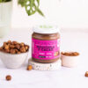 barattolo di crema crunchy nocciola e cacao su una base effetto granito con ciotola di nocciole a sinistra e di cacao a destra, vaso con pianta sullo sfondo