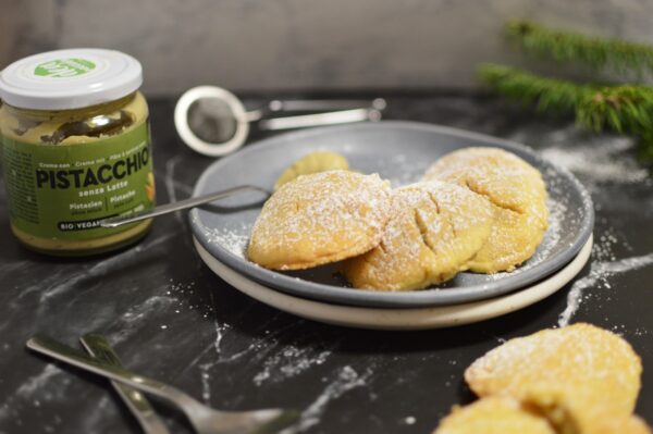 piatto con biscotti al cuor di pistacchio, nello sfondo altri biscotti e un barattolo di pistacchio vegan